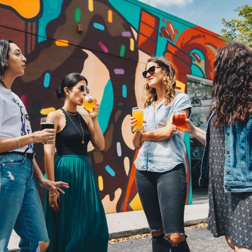 A group of young people enjoying alcoholic beverages in front of a graffiti wall
