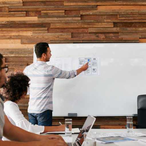 Man writing on a white board while co-workers watch.