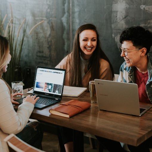 Co-workers at a desk discussing work while smiling.