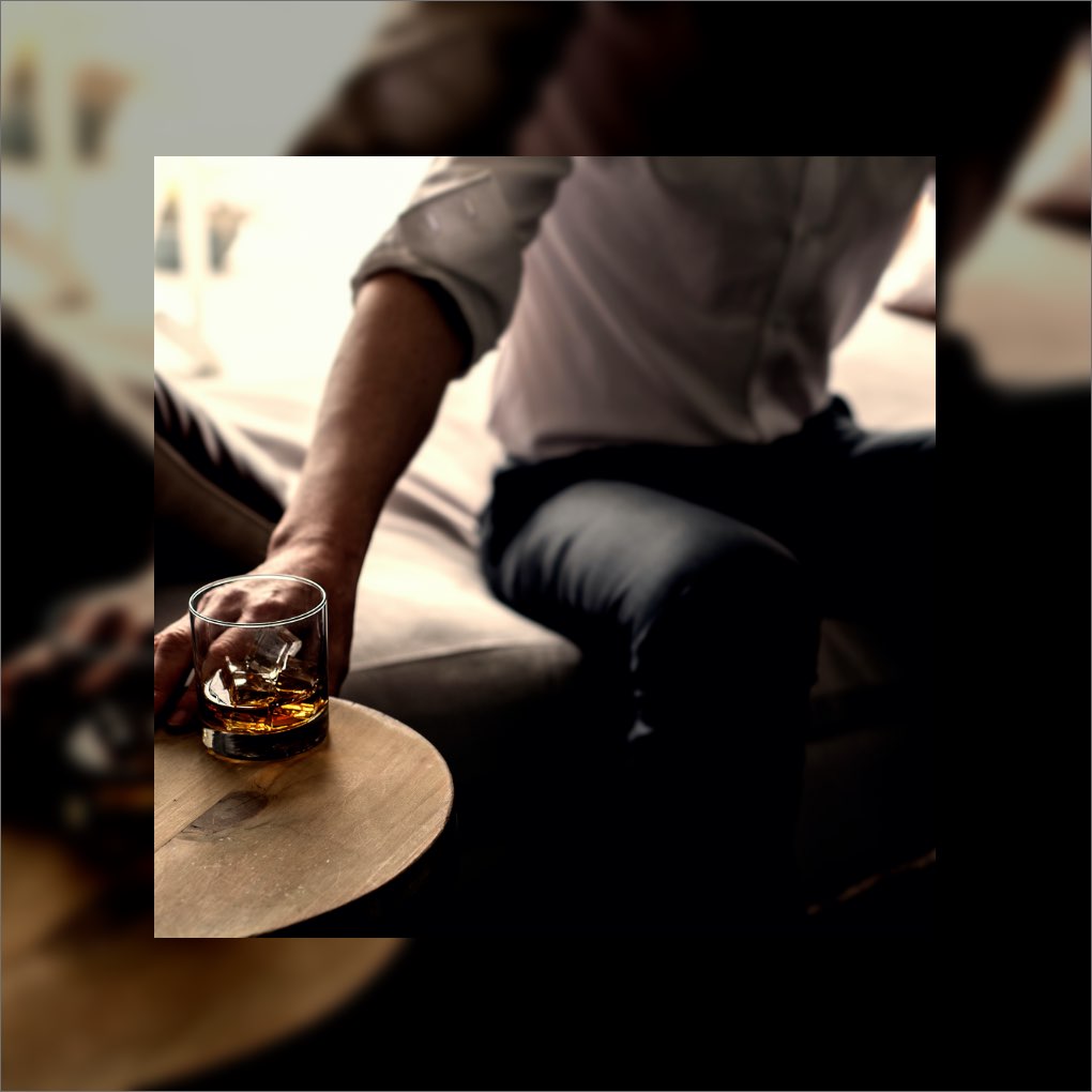 A man reaching for a glass of whiskey on the rocks.